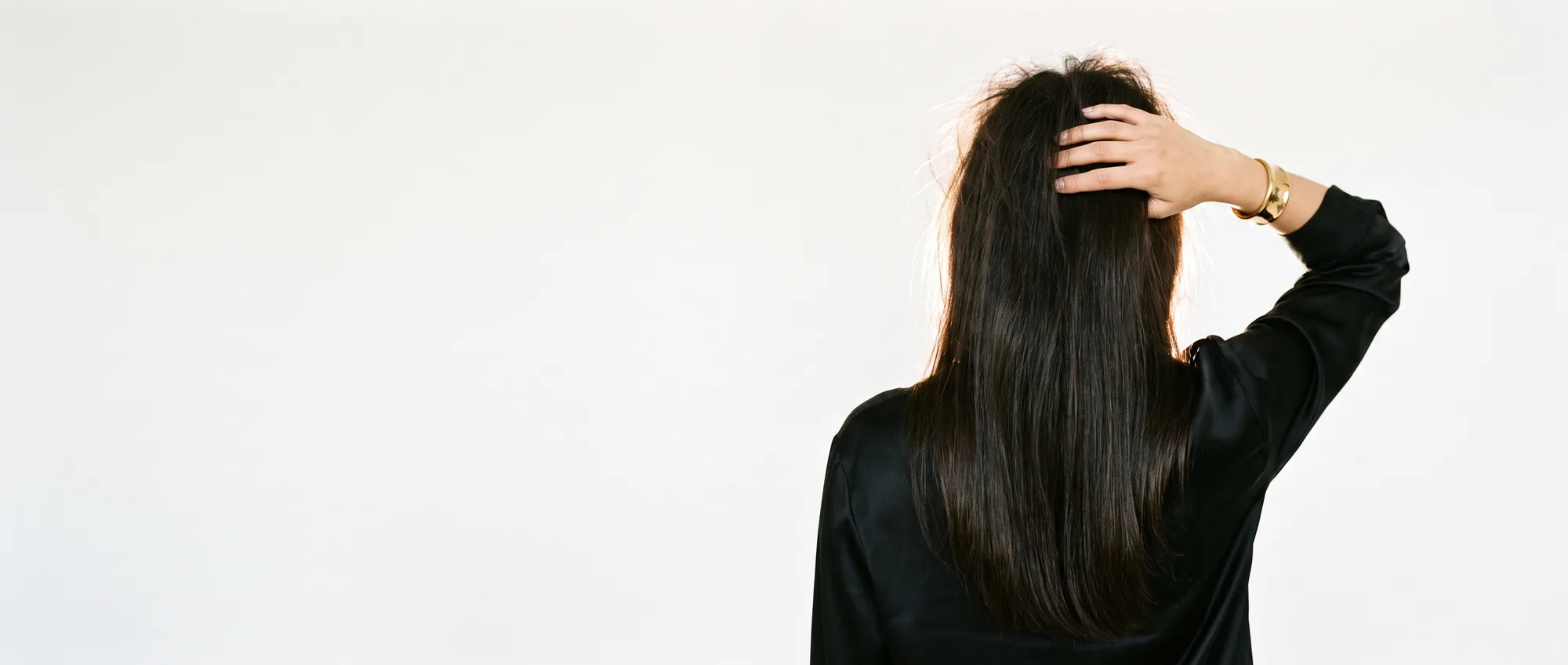Una donna di spalle liscia con la mano i capelli scuri, leggermente crespi in cima, su sfondo bianco