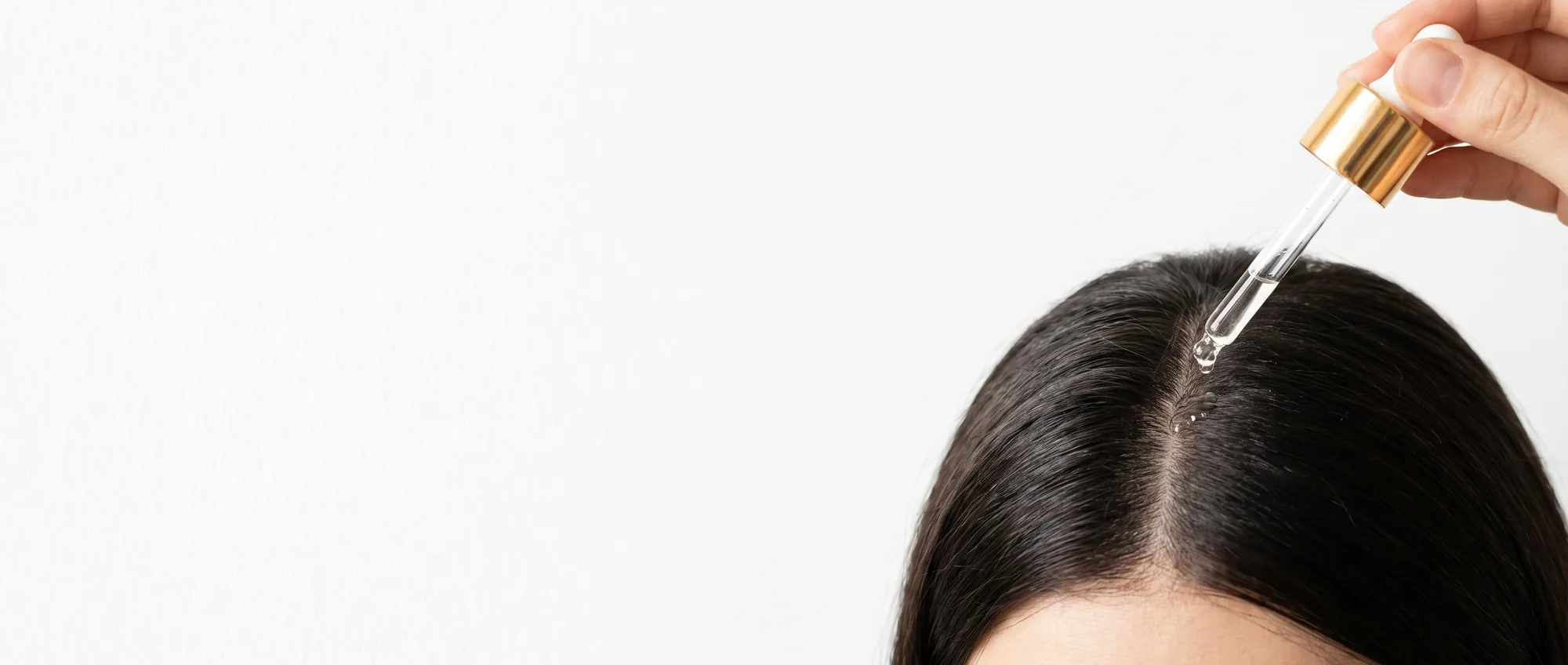 Una pipetta dorata applica qualche goccia di siero sulla cute lungo la riga dei capelli scuri