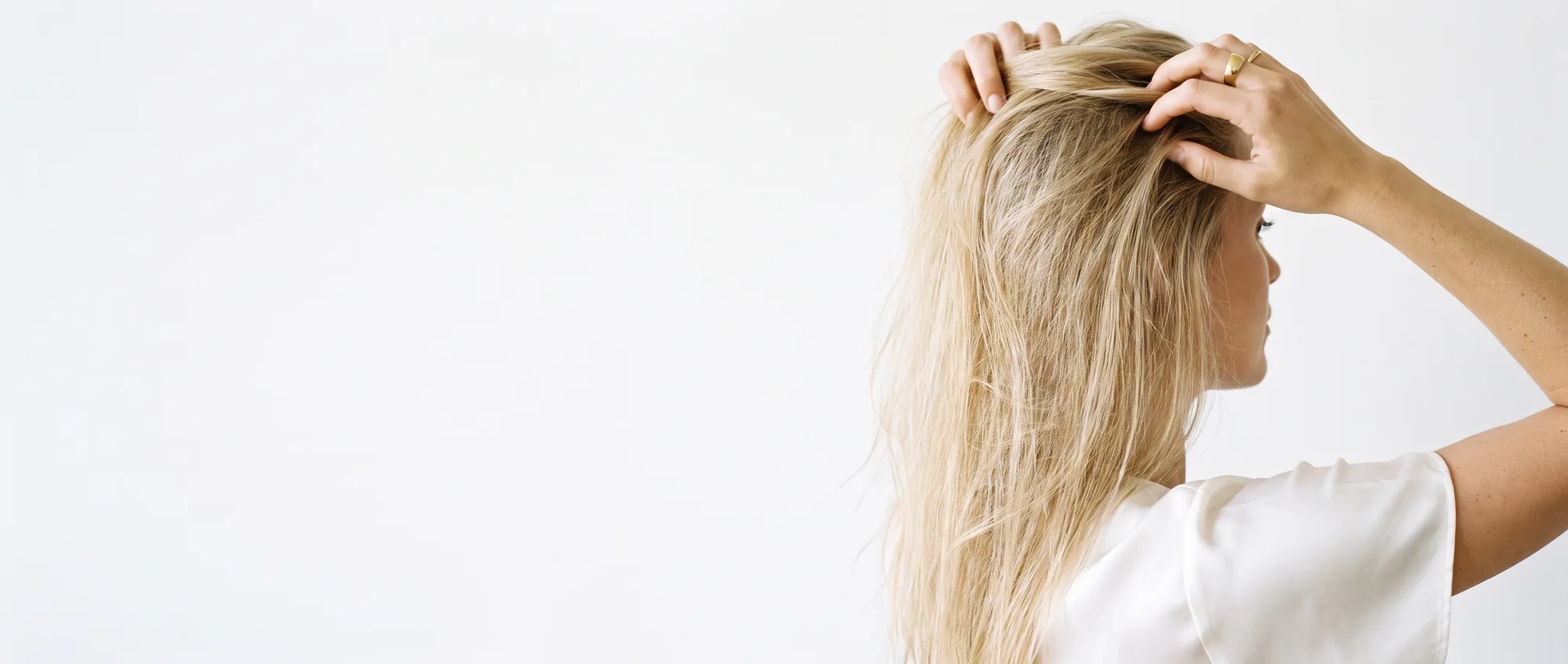 Una donna solleva alla radice i capelli biondi fini e leggeri, su sfondo bianco