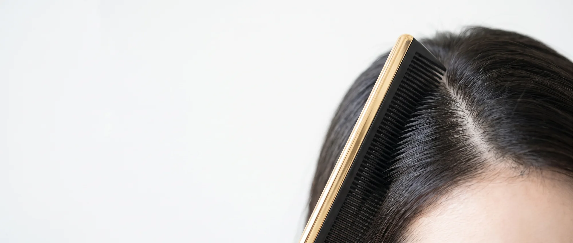 Un pettine nero e oro separa i capelli scuri alla radice, mostrando la cute