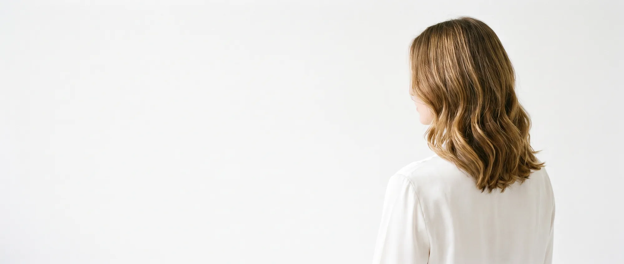 Una donna di spalle con capelli mossi castano chiaro a onde morbide, su sfondo bianco