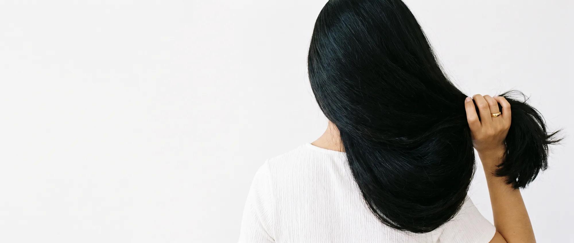 Una donna di spalle raccoglie su una spalla i capelli neri lunghi, spessi e folti