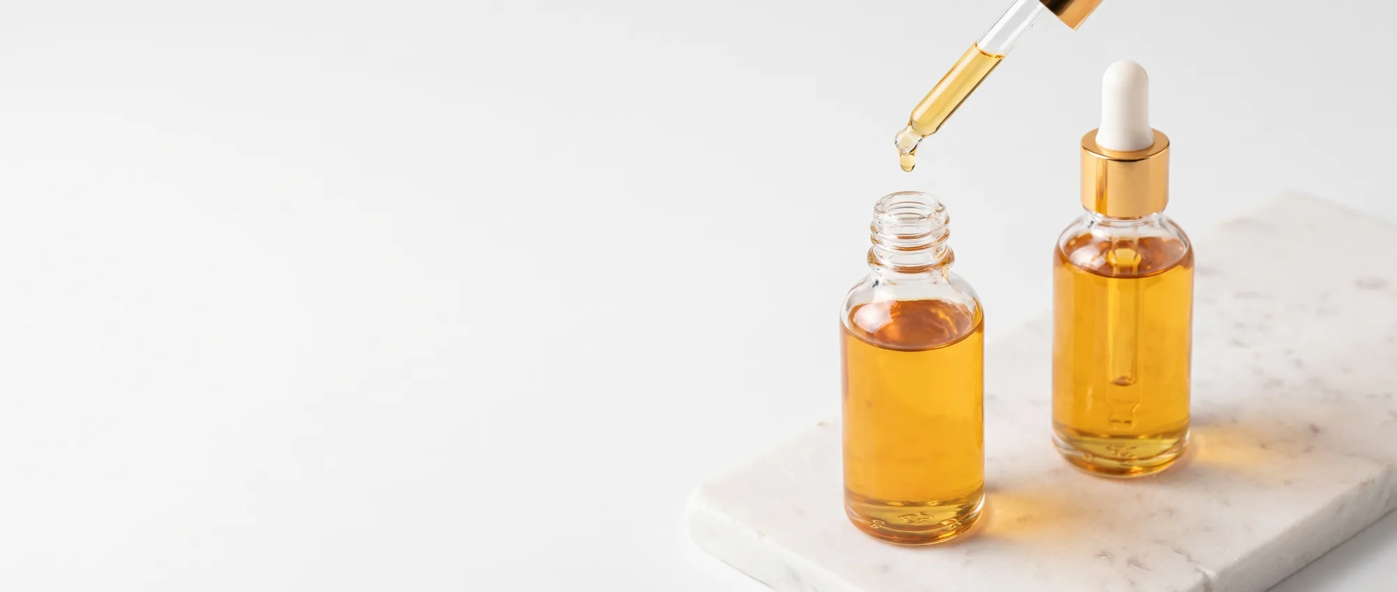 Flaconi di olio e siero per capelli in vetro su una superficie bianca con dettagli dorati