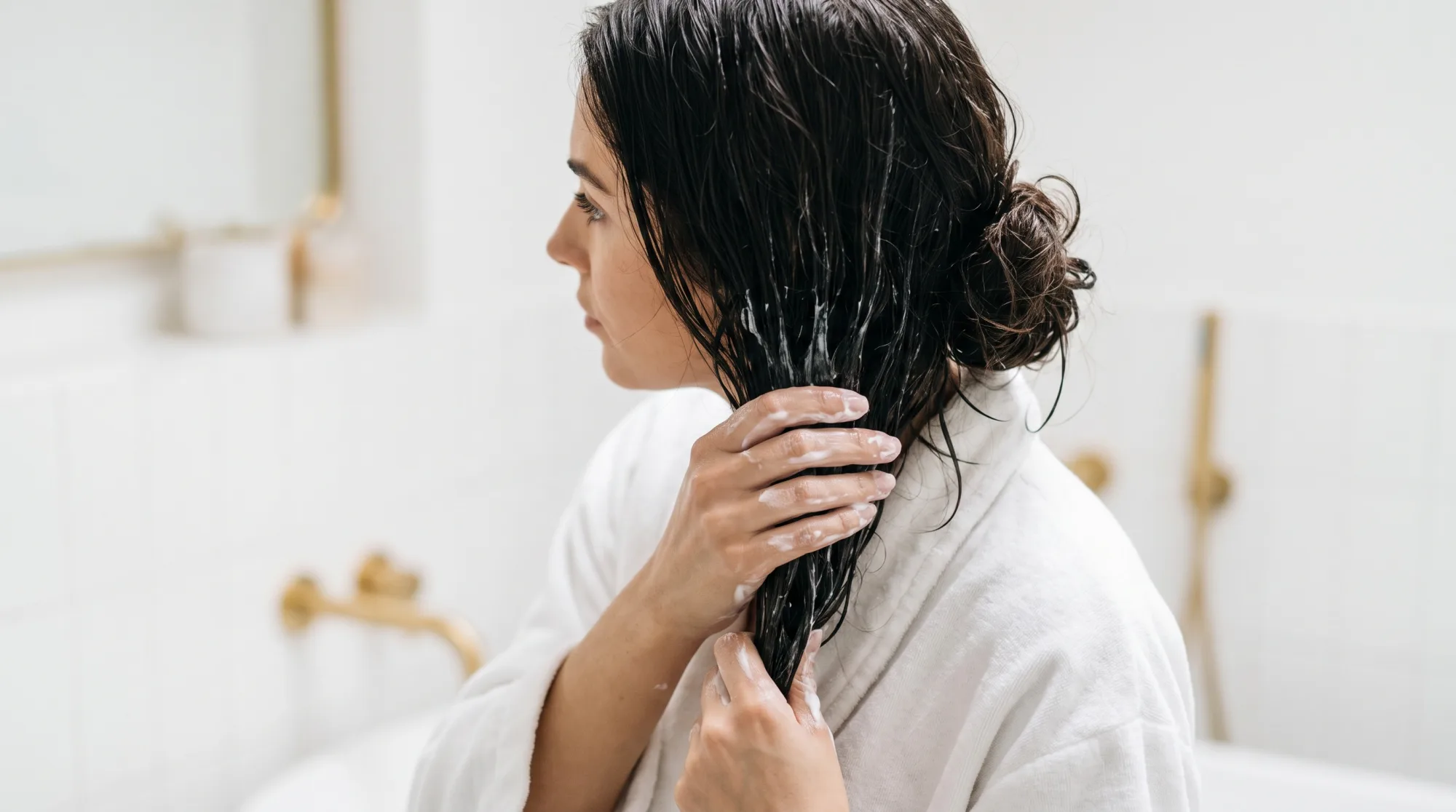 Una mano preleva una noce di maschera per capelli da un vasetto bianco con dettagli oro